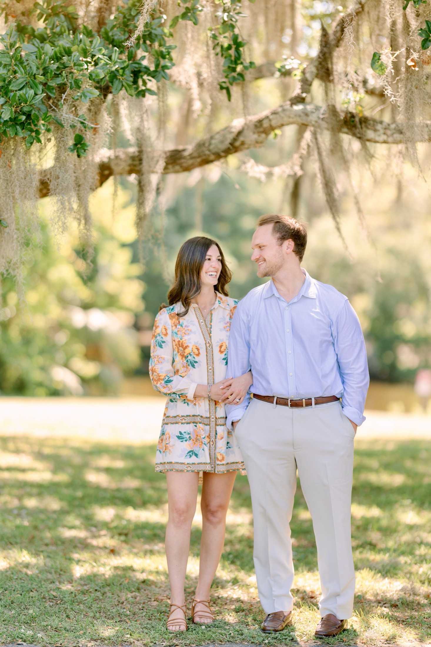 A newly engaged couple smiling beneath live oaks and Spanish moss