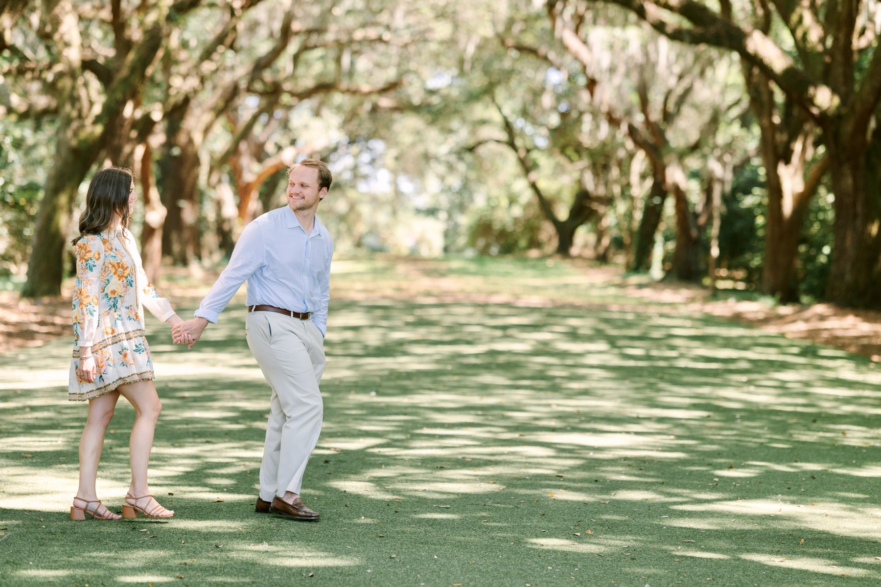 The couple walking hand in hand beneath a canopy of oak trees